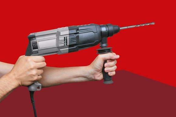 Eine Person hält einen Bohrhammer mit beiden Händen vor einem roten Hintergrund.